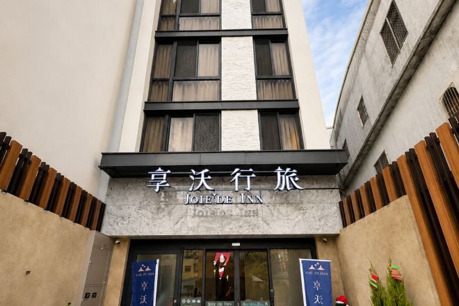 A hotel entrance with a sign reading 'JOIE DE VINNE' and a modern facade.