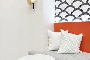 Een moderne kamer met een grijze bank, witte kussens en een behang met een patroon.