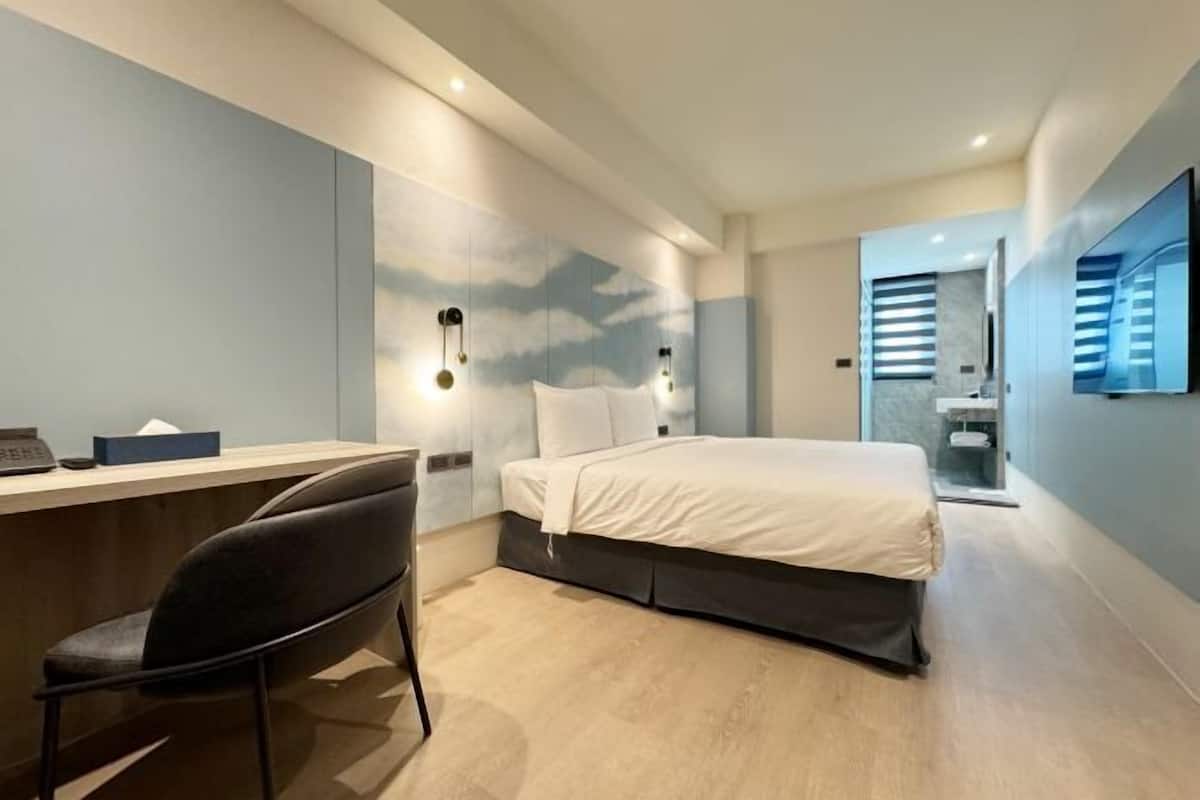 A modern hotel room with a desk, a bed, and a bathroom.