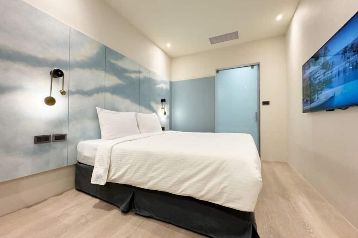 A modern bedroom with a bed, a wall-mounted light fixture, and a door.