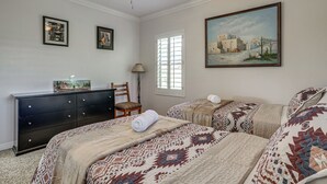 Un dormitorio con dos camas, un tocador, una silla, un cuadro y una ventana.