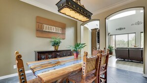 A dining area with a long wooden table, chairs, a chandelier, a painting on the wall, and a view through an archway to an outdoor area. - Mtn-View Patio Oasis! Luxe Family Home in Peoria (Peoria)