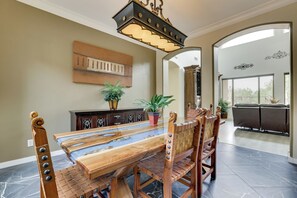 A dining area with a long wooden table, chairs, a chandelier, a painting on the wall, and a view through an archway to an outdoor area. - Mtn-View Patio Oasis! Luxe Family Home in Peoria (Peoria)