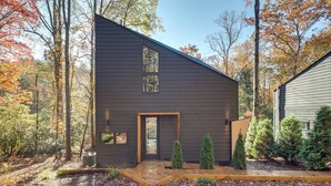 Una casa moderna con fachada oscura, puerta de madera y un ventanal pequeño.