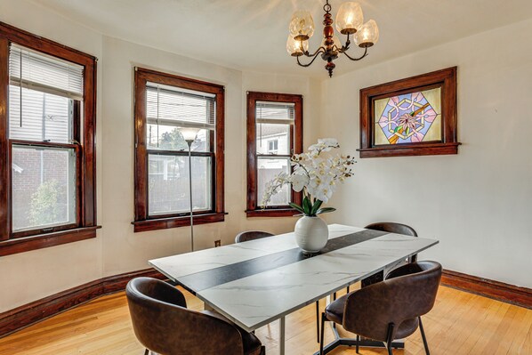 Uma sala de jantar com uma mesa de mármore, quatro cadeiras, um vaso com flores e uma janela de vitral.