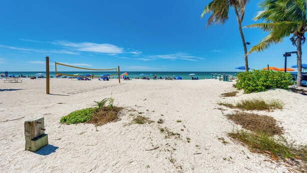 A beach volleyball net, palm trees, and beach umbrellas. - Stroll to Bonita Beach Park: Ocean-View Getaway (Bonita Springs)