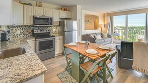 A modern kitchen with granite countertops, stainless steel appliances, and a dining area with a wooden table and chairs. - Stroll to Bonita Beach Park: Ocean-View Getaway (Bonita Springs)