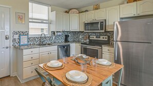 A kitchen with white cabinets, a stainless steel refrigerator, a microwave, and a stove. There is a dining table set with plates and glasses. - Stroll to Bonita Beach Park: Ocean-View Getaway (Bonita Springs)