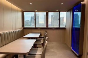 A conference room with a long table and chairs, large windows with blinds, and a view of buildings.