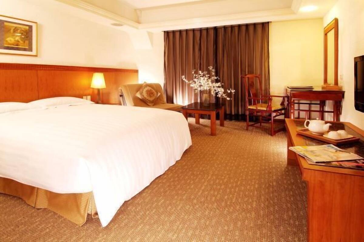 Habitación de hotel con una cama grande, un escritorio con lámpara, una silla, un televisor y una cortina.
