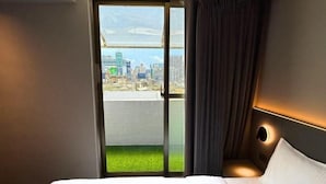 A hotel room with a bed, a city view through a sliding door, and a nightstand with a lamp. - Hub Hotel Ximen-Kunming Branch (Taipei)