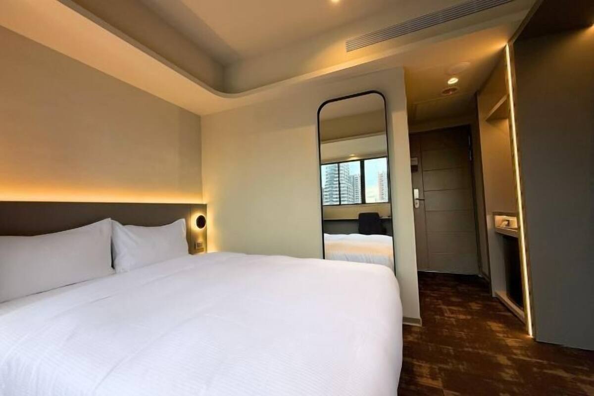 Habitación de hotel con una cama grande, un espejo, una mesita de noche y vistas al pasillo.