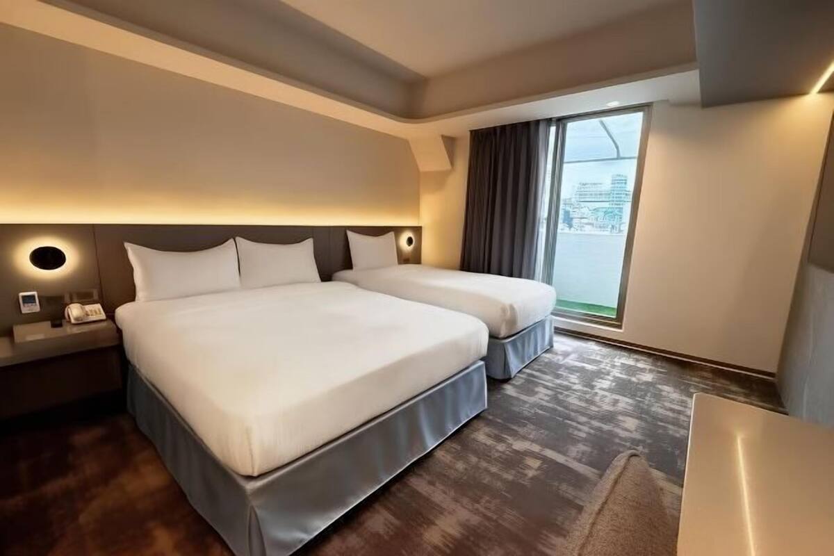 Habitación de hotel con dos camas, un ventanal grande y vista a la ciudad.