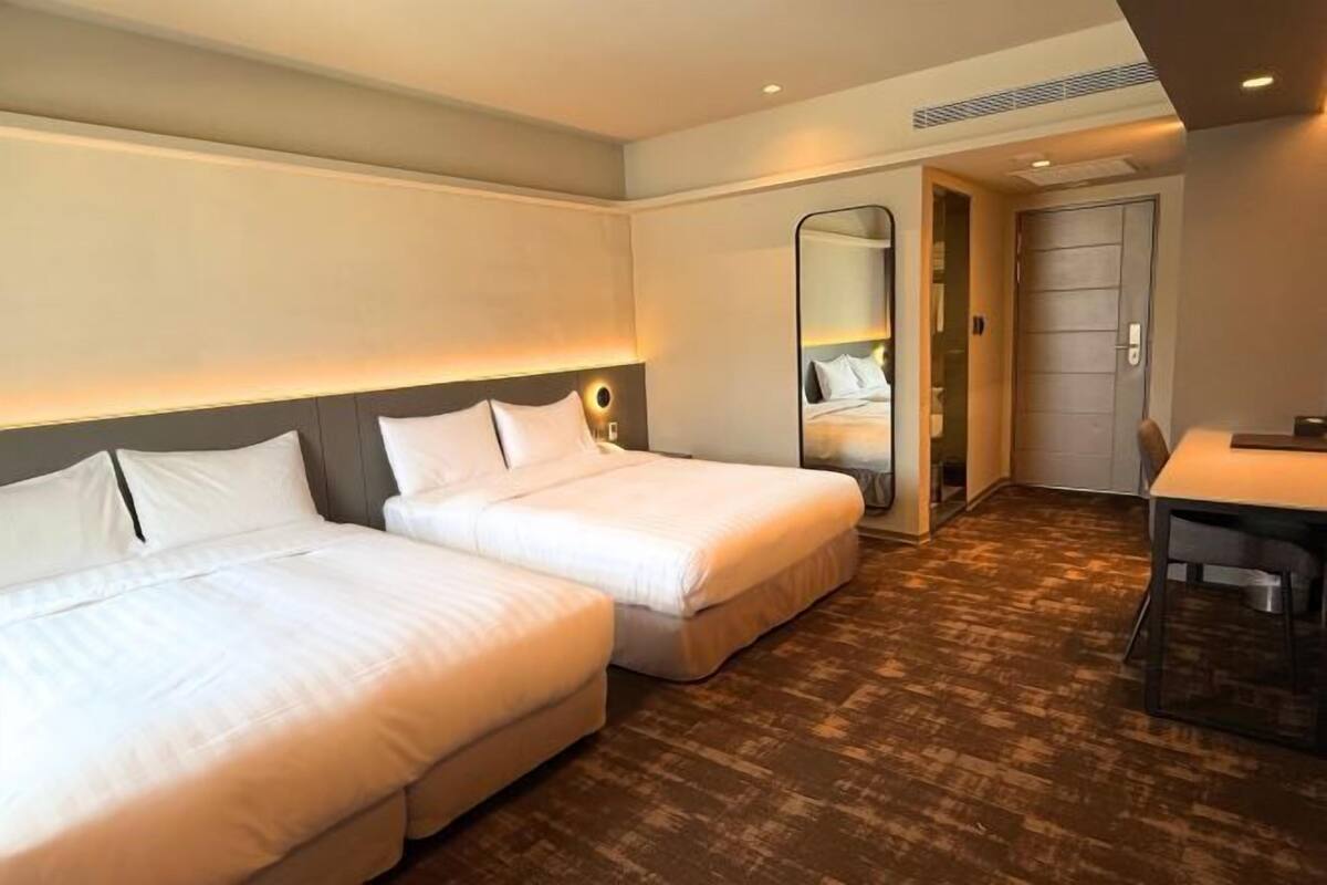 Una habitación de hotel con dos camas, un escritorio y un espejo.