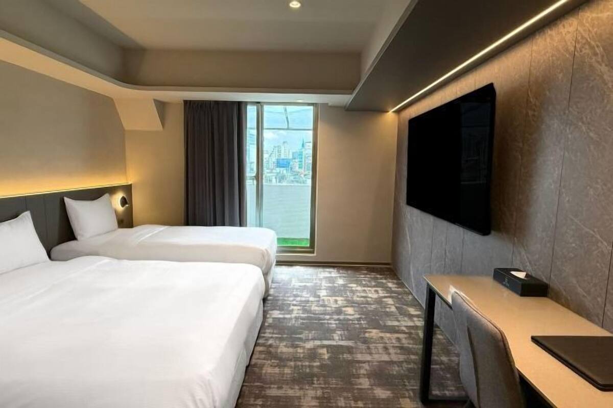 Habitación de hotel con dos camas, un escritorio, televisión de pantalla plana y vista a la ciudad.