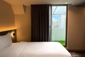 A hotel room with a bed, a headboard with a light fixture, a large window with a view of buildings, and a curtain. - Hub Hotel Ximen-Kunming Branch (Taipei)