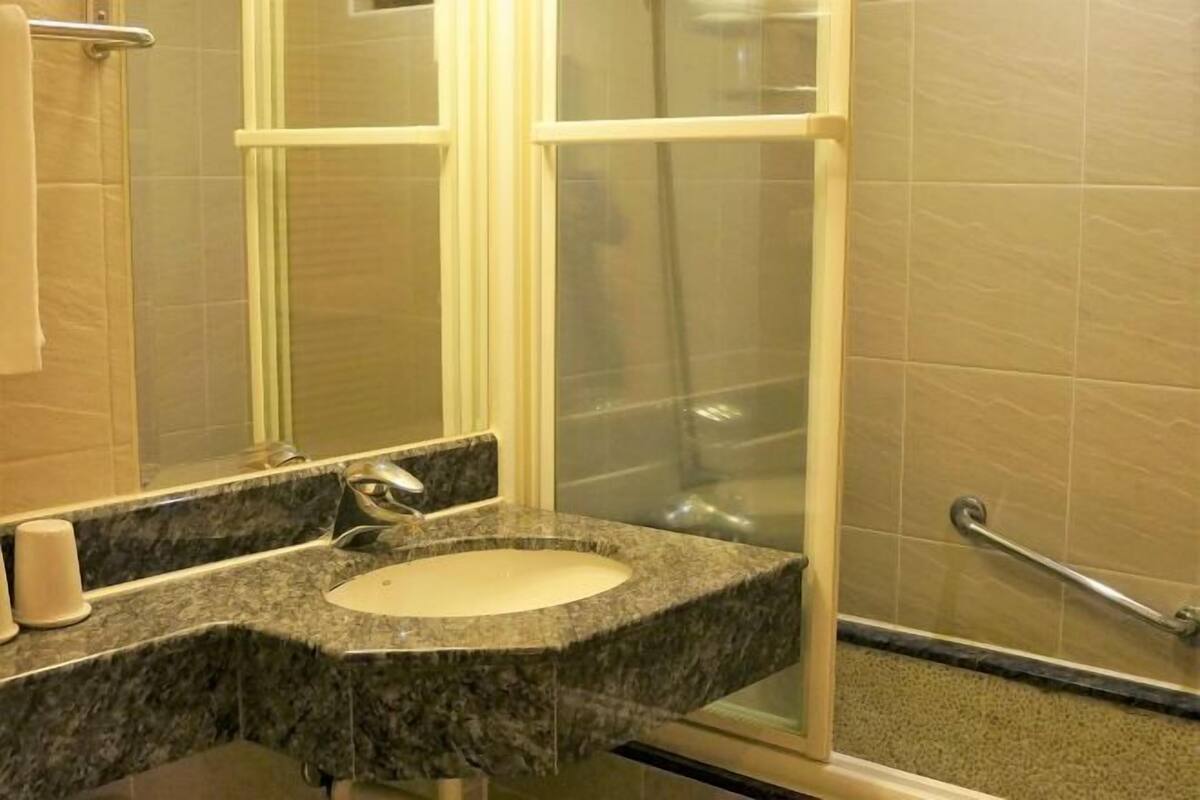 Un baño con lavamanos de granito, un espejo, cabina de ducha con mampara de vidrio y pasamanos.