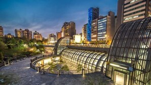 A modern hotel with a curved glass facade, a central courtyard, and a view of surrounding high-rise buildings. - Hub Hotel Ximen-Kunming Branch (Taipei)