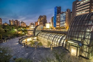 A modern hotel with a curved glass facade, a central courtyard, and a view of surrounding high-rise buildings. - Hub Hotel Ximen-Kunming Branch (Taipei)
