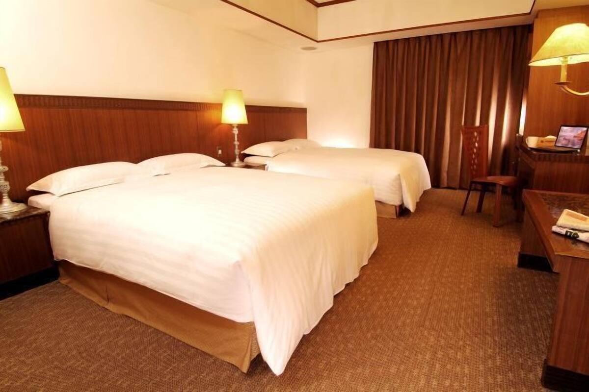 Una habitación de hotel con dos camas, un escritorio con lámpara y una silla.