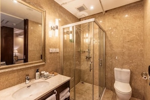 Un baño con lavamanos de mármol, ducha con mampara de vidrio y retrete.