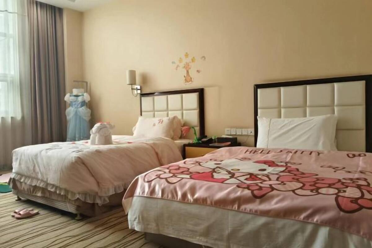 A hotel room with two beds, a nightstand, a lamp, a wall decoration, and a window with curtains.