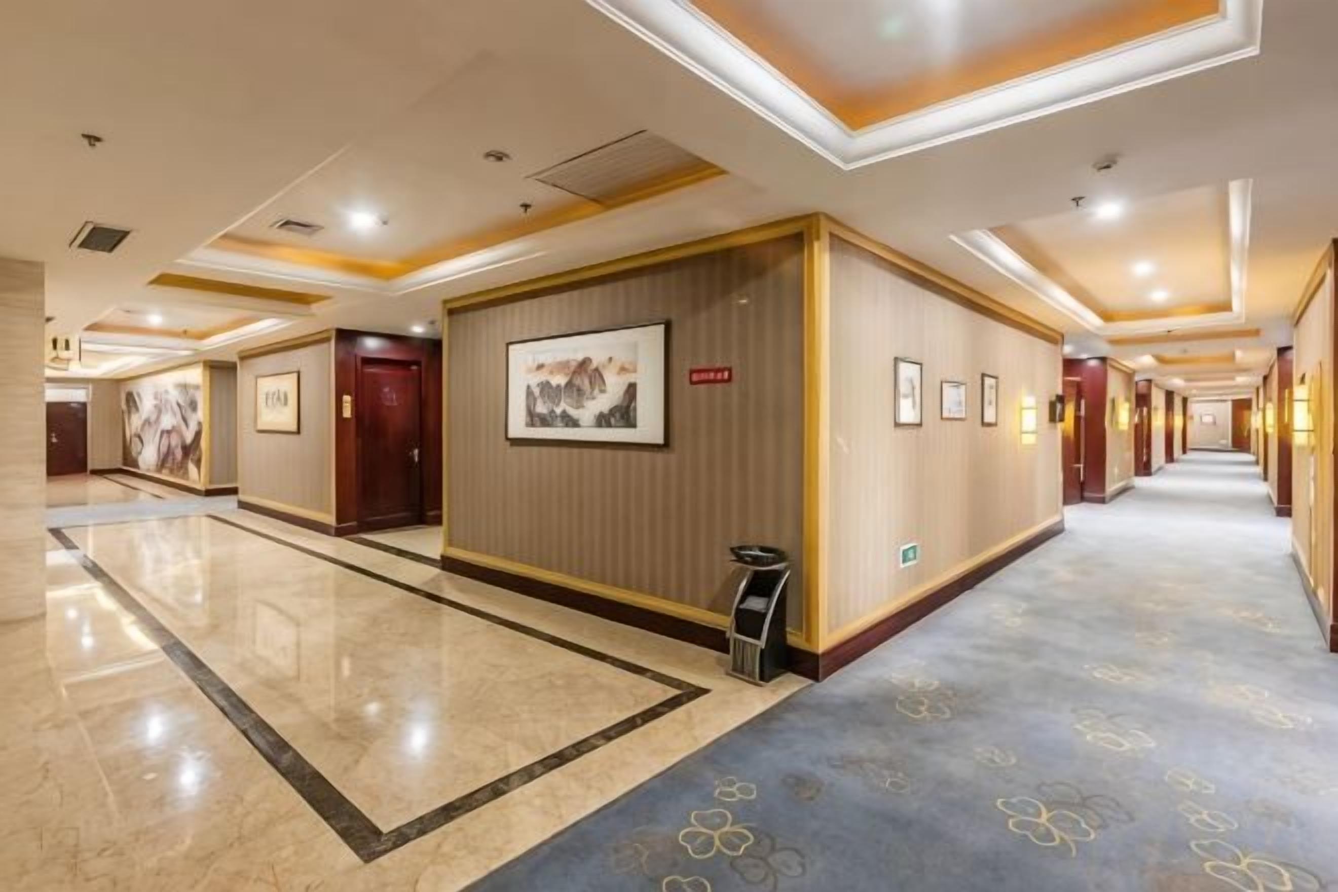A hotel corridor with framed artwork on the walls, a carpeted floor, and a reception desk.