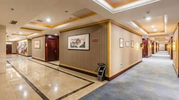 A hotel corridor with framed artwork on the walls, a carpeted floor, and a reception desk.