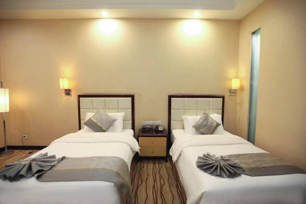 A hotel room with two beds, bedside tables, lamps, and a carpeted floor.