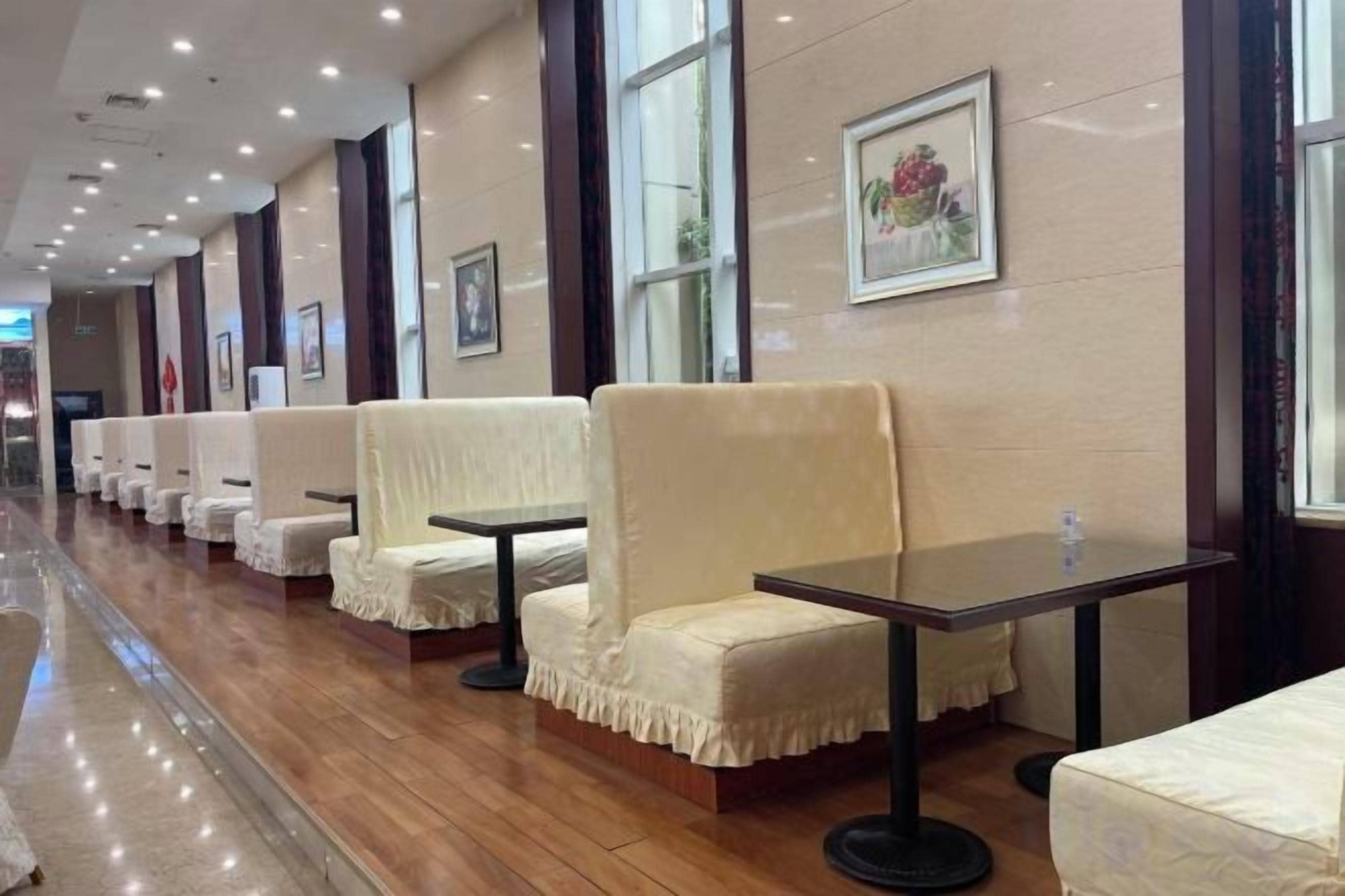 A row of cream-colored chairs and tables in a hotel lobby with a polished wooden floor and a large window.