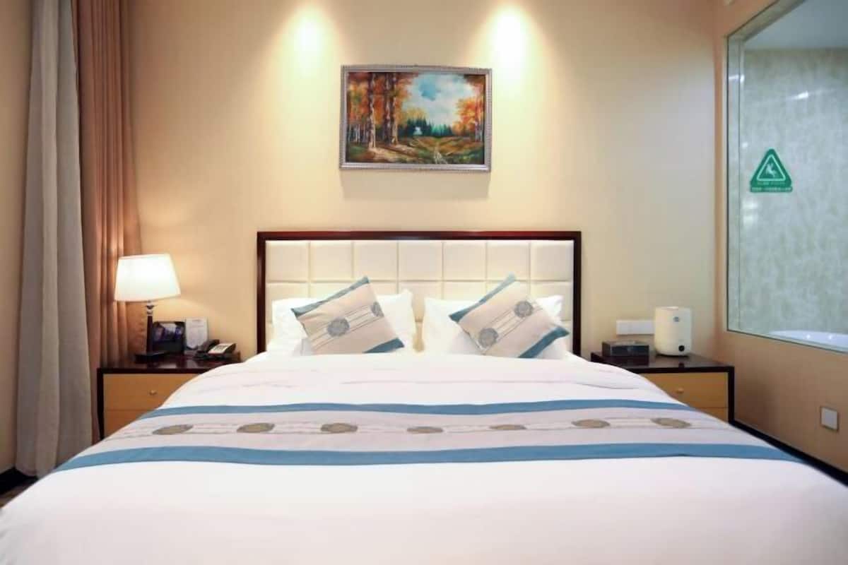 A hotel room with a bed, a nightstand with a lamp, a painting on the wall, and a window with a safety sign.