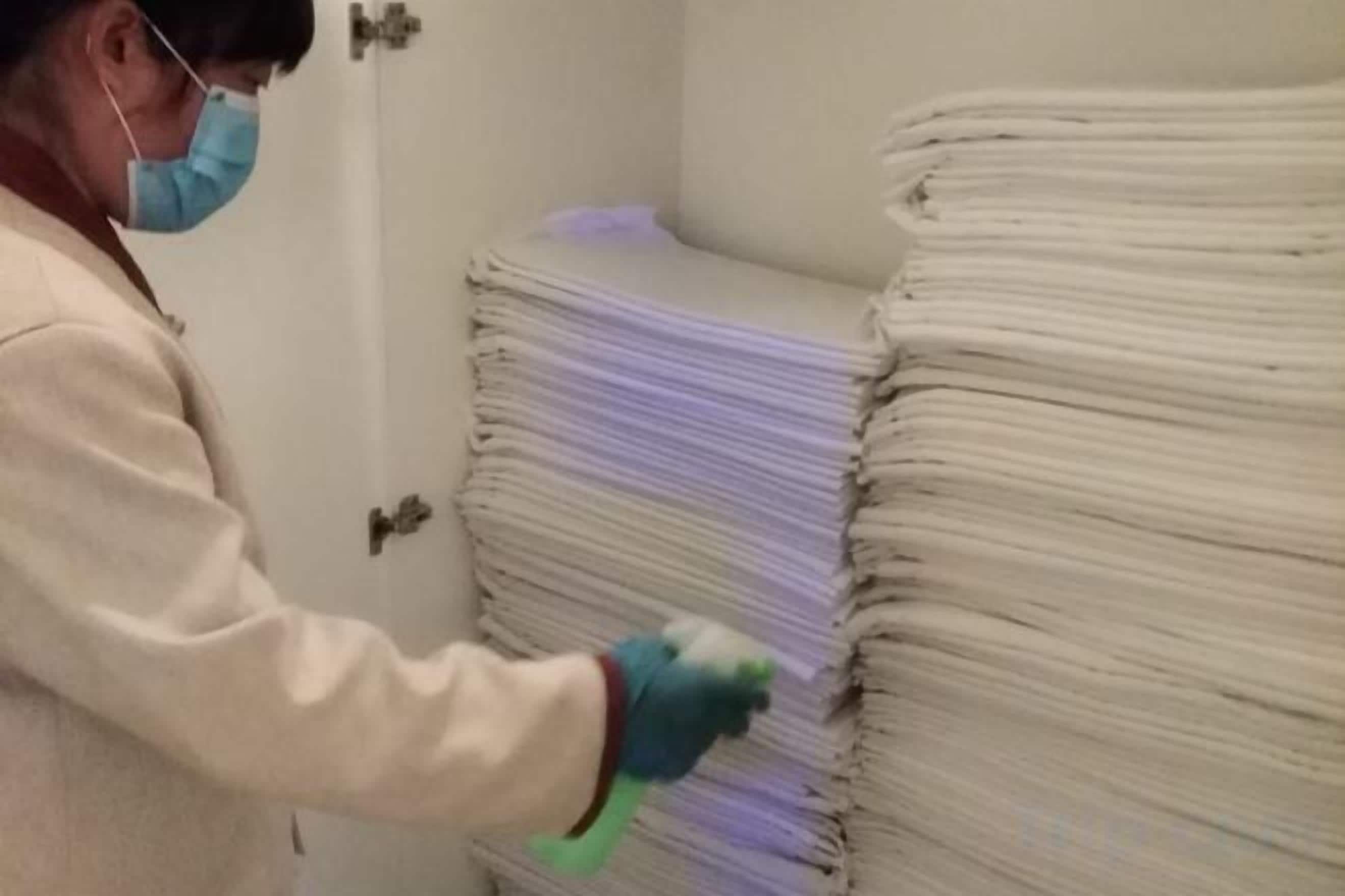 A person wearing gloves handling a stack of white objects, possibly in a storage or processing area.