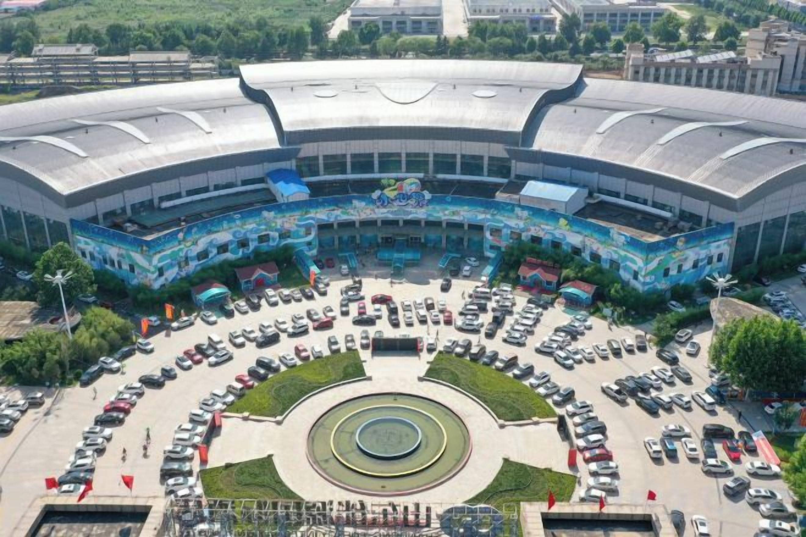 Um estádio grande com uma praça circular central e estacionamento ao redor.