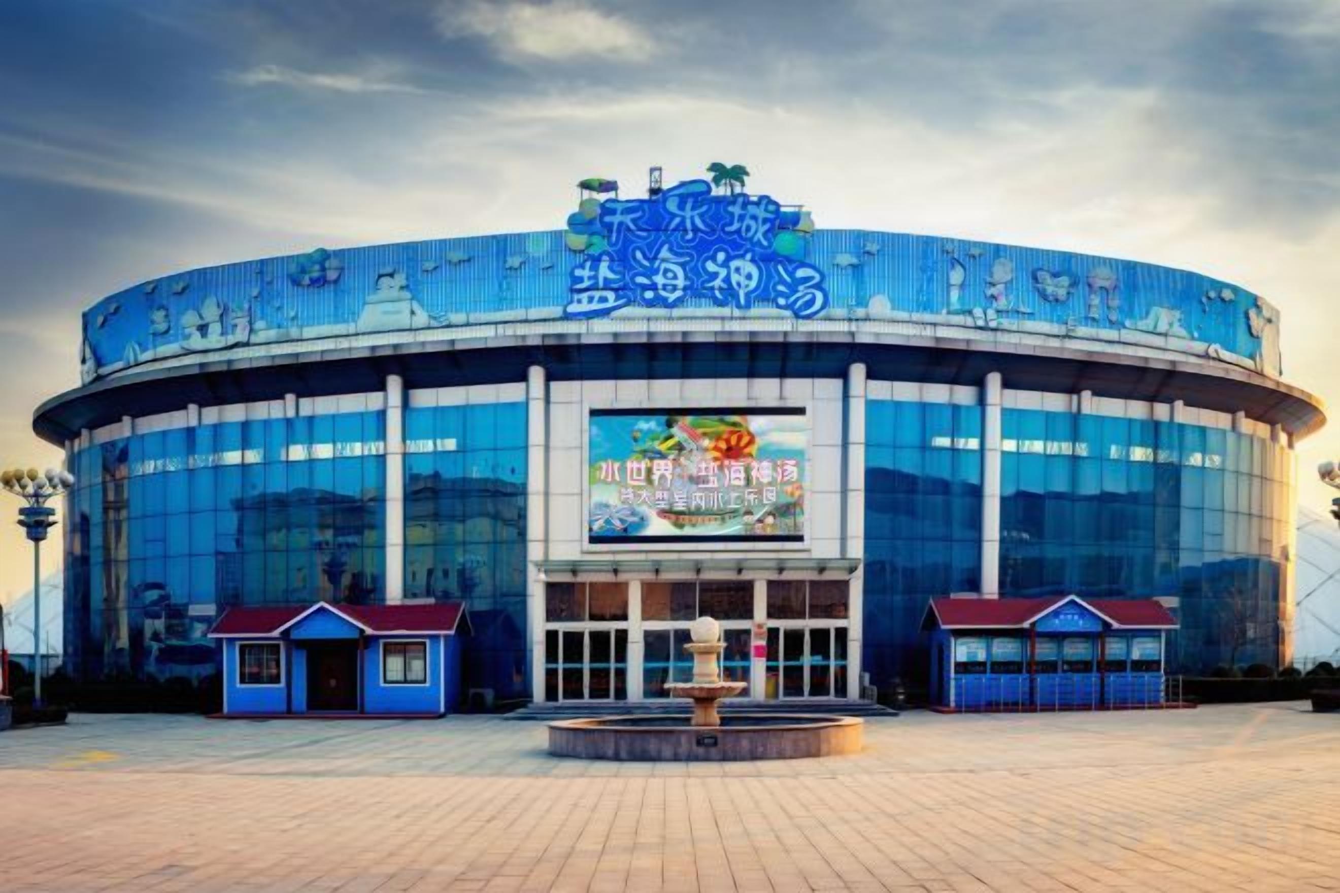 A large, modern building with a curved facade, large glass windows, and a prominent entrance with a blue roof.