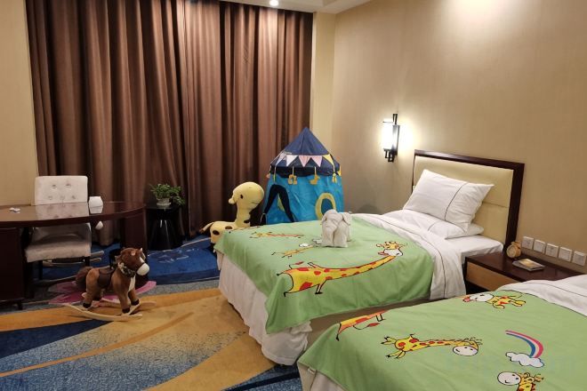 A hotel room with two beds, a desk, a chair, a small table, and a play tent.