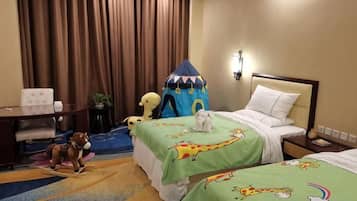 A hotel room with two beds, a desk, a chair, a small table, and a play tent.