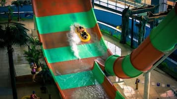 A water slide with a person at the top, indoor pool area, and a lifeguard stand.
