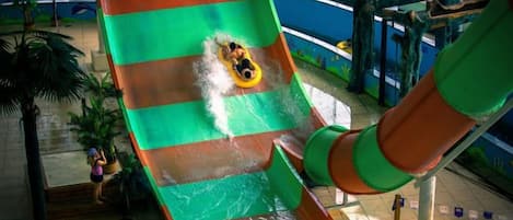 A water slide with a person at the top, indoor pool area, and a lifeguard stand.