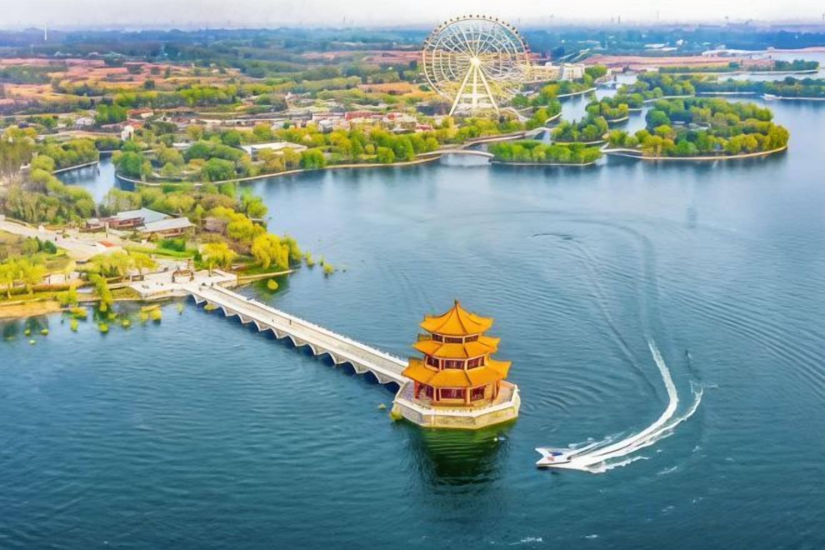A water body with a traditional building on a small island, a bridge, and a Ferris wheel in the background.