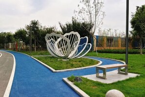 Un sendero con superficie azul, una escultura abstracta blanca y un banco.