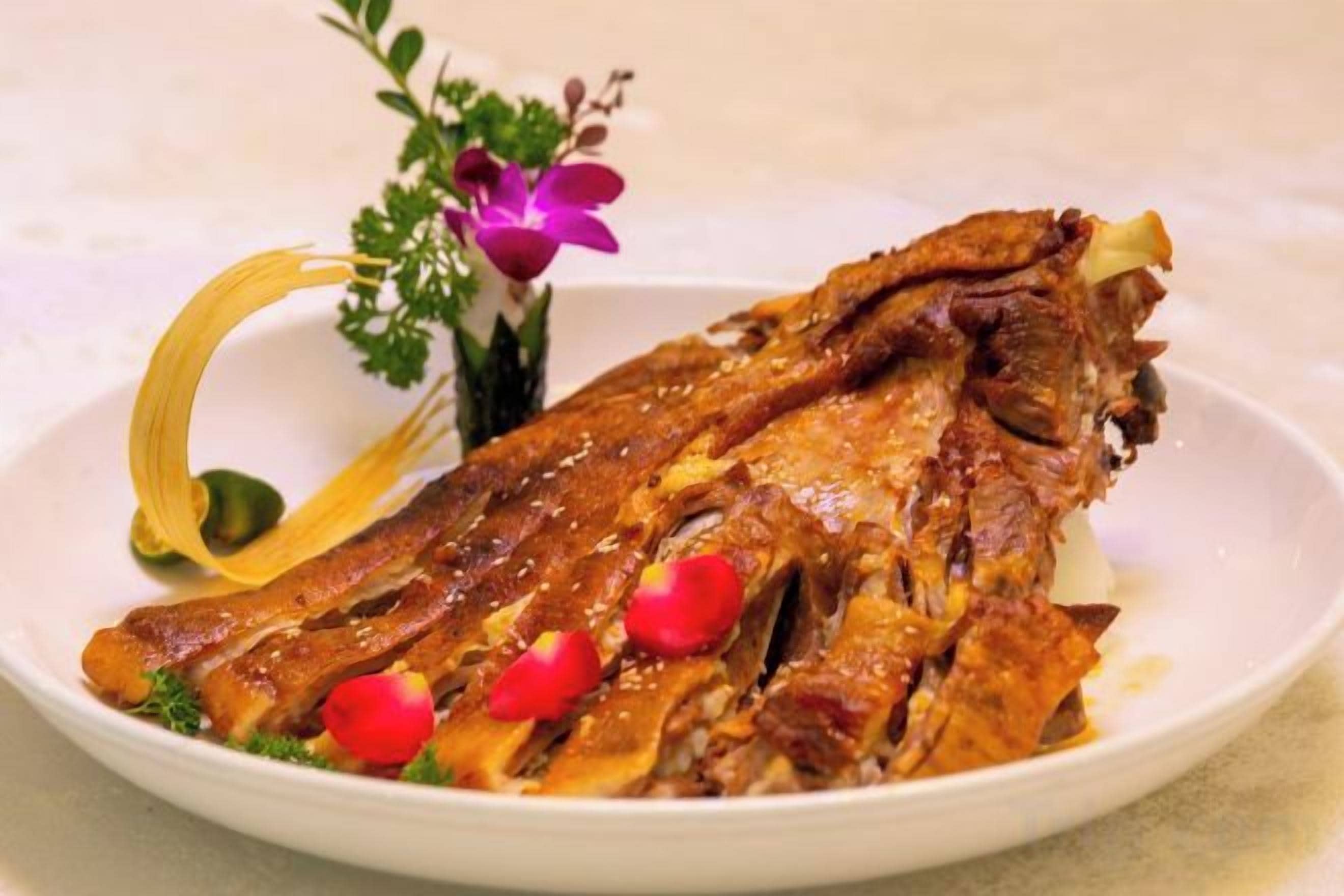 A plate with a cooked fish, garnished with red chili peppers and a decorative flower arrangement.