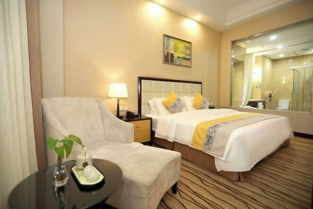 A hotel room with a bed, a chair, a nightstand, a lamp, a mirror, and a painting on the wall.