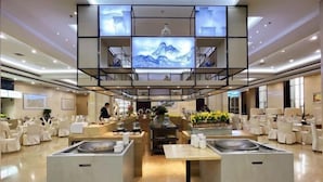 Un moderno vestíbulo de hotel con una zona de estar central, una gran pantalla digital y una mesa de buffet.