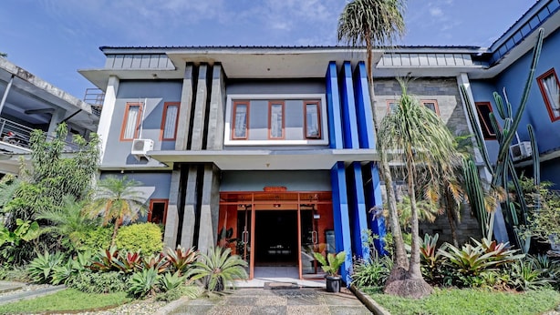 Un bâtiment moderne avec une entrée en verre, entouré de plantes tropicales et bordé d’un chemin de gravier.