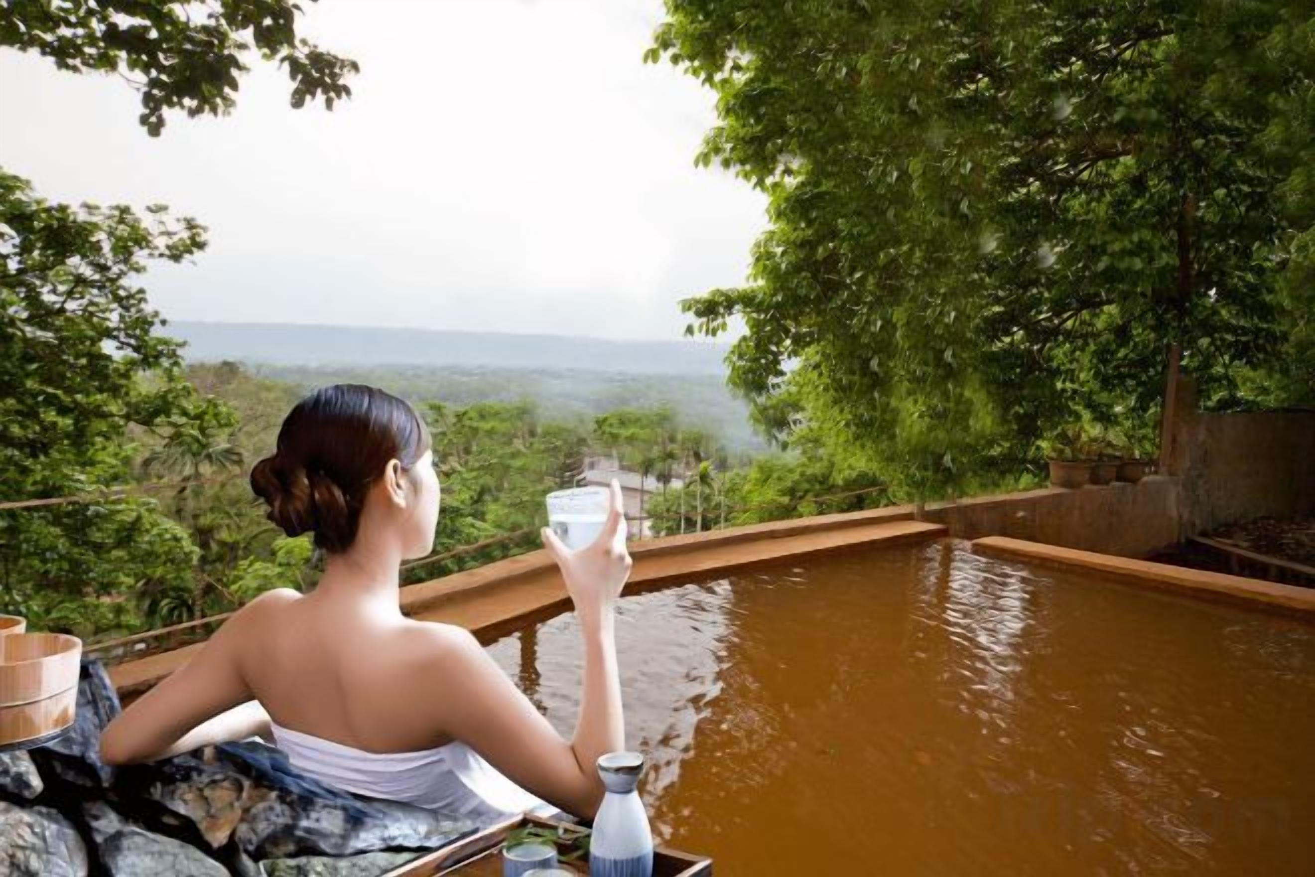 Una persona relaxant-se al costat d'una piscina de fusta amb vista a un paisatge boscós.