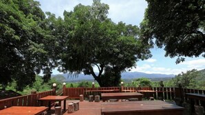 An outdoor wooden deck with tables and chairs, surrounded by trees and a view of the landscape. - Juei-Suei Hotspring (Hualien)