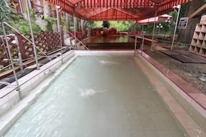 Une piscine surmontée d’un auvent rouge, entourée d’une clôture en bois et agrémentée d’une petite cascade.