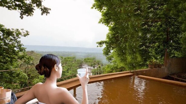 A person sitting by a wooden pool with a view of a forested landscape. - Juei-Suei Hotspring (Hualien)
