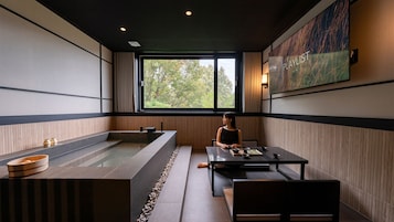 A modern spa room with a large bathtub, a table with tea set, and a painting on the wall.