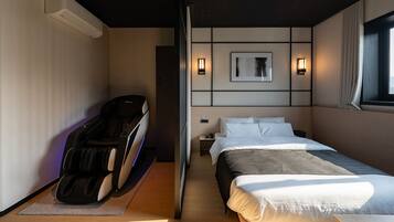 Habitación de hotel con sillón de masaje, cama con ropa de cama blanca, mesita de noche y una obra de arte colgada en la pared.